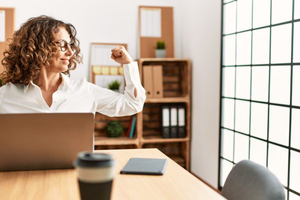 Middle age hispanic woman working at the office wearing glasses showing arms muscles smiling proud. fitness concept. Middle age hispanic woman working at the office wearing glasses showing arms muscles smiling proud. fitness concept.
